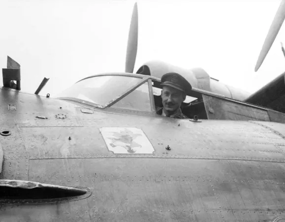 A black-and-white image shows a young male pilot in uniform, smiling as he looks out of the cockpit of an aircraft.