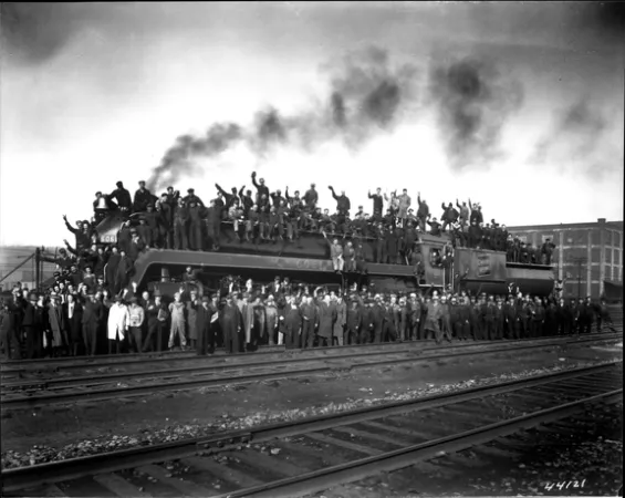 : L’image est une photo noir et blanc montrant des ouvriers qui posent sur une locomotive et tout autour pour faire la promotion des obligations de la Victoire.
