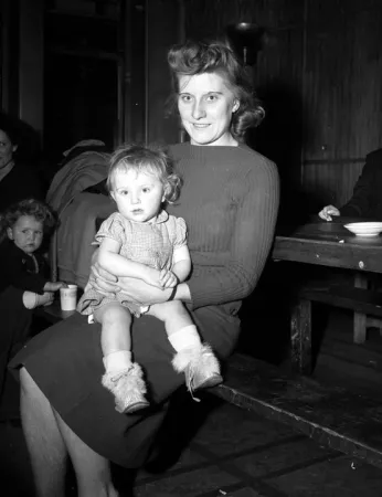 Image is a black-and-white photograph of a woman holding a child on her knee.