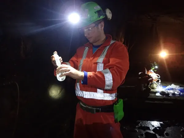 A researcher in orange coveralls and a headlamp prepares a sample underground.
