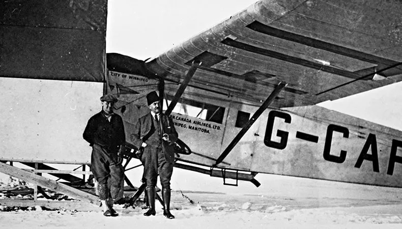 Une image en noir et blanc montre une scène hivernale d'un avion chargé par des hommes, avec plusieurs grands sacs de courriers alignés prêts à être expédiés.