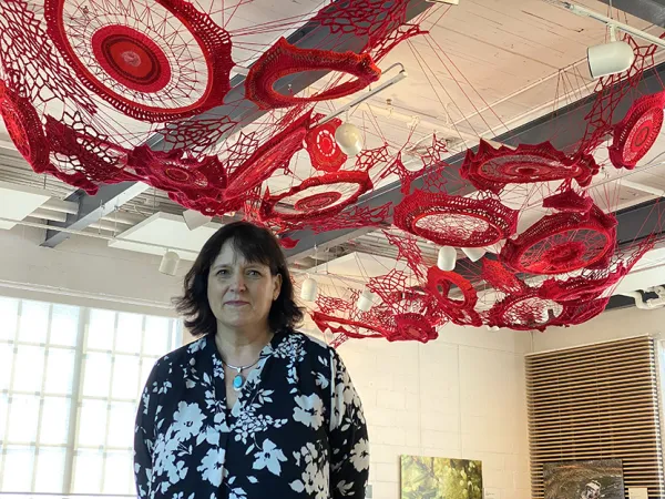 Tracey-Mae Chambers stands under her art installation made of red and orange yarns at the Canada Agriculture and Food Museum.