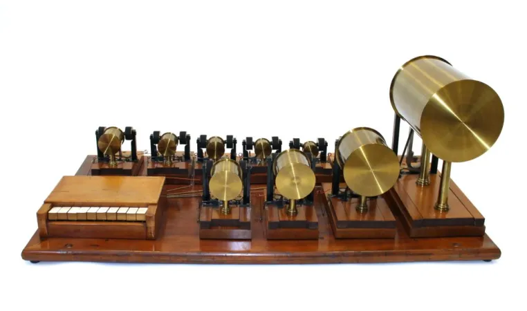 Table-top instrument featuring a small 10-key keyboard made of wood and ivory and ten cylindrical resonators made of brass. All are mounted on a wooden base.