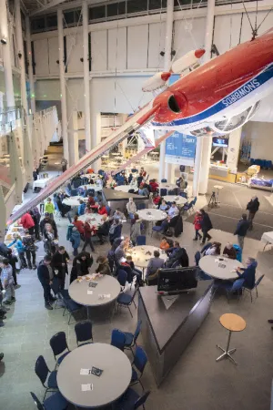 A view inside the Canada Aviation and Space Museum's lobby during an event. People are sitted on round tables around the room. 
