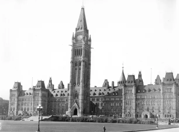 A black and white photograph of a large, stone building with large tower in the centre.