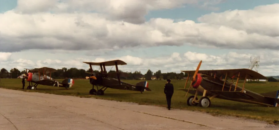 Three old airplanes are lined up, facing forward, along the edge of a paved runway for public viewing.