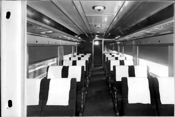 L’image est une photo noir et blanc montrant l’intérieur d’un wagon de passagers tout neuf et sans passagers.