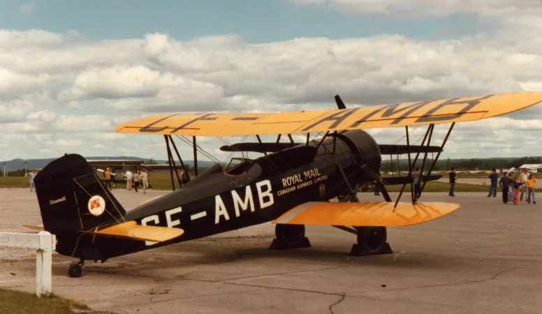 A mid-sized biplane with distinctive yellow wings, photographed outdoors from the back right.