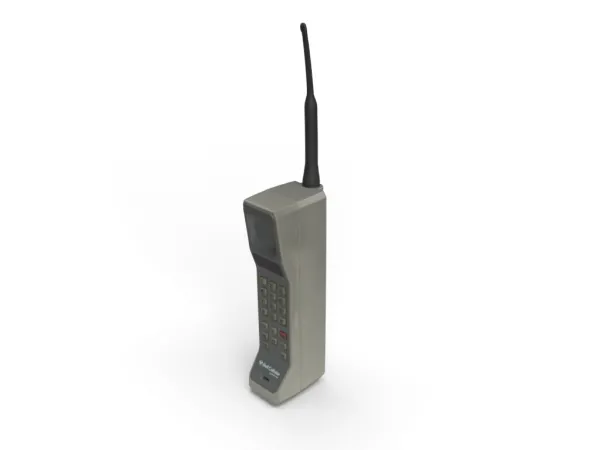 Un vieux téléphone cellulaire gris ressemblant à une brique avec une grande antenne et de larges côtés. Il est doté de boutons-poussoirs physiques et de zones où écouter et où parler devant l’appareil.
