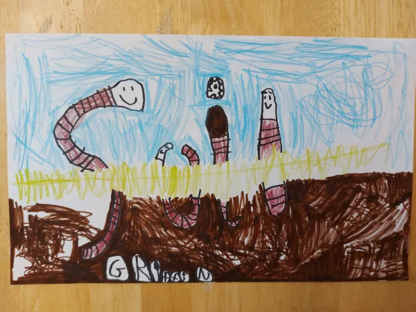  Un dessin d’enfant coloré présentant quatre joyeux vers de terre sortant de la terre. Leurs corps sont dessinés pour former le mot « soil » (sol). 