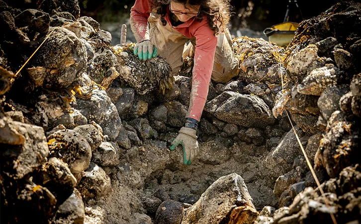 Photograph of a women reaching into a pile of dirt and rocks.