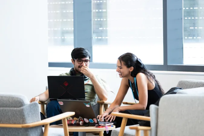 Deux participants souriant et regardant le même écran d'ordinateur près d'une grande fenêtre.