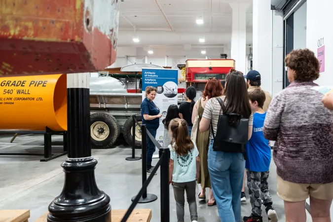 A group of adults and children touring the Ingenium Centre and standing in the Ingenium collection listening to a guide.