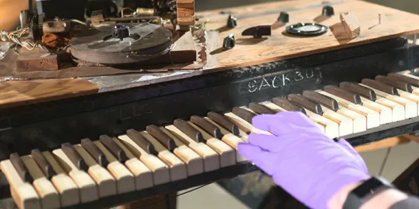Une main gantée joue sur le clavier d’un synthétiseur appelé la saqueboute électronique.