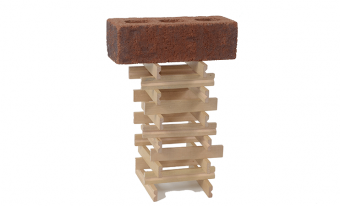 Wooden sticks are stacked, two on each layer and alternating direction in each layer to form a square based tower with a hollow centre. A brick sits atop the tower.