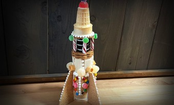 An edible rocket, made with cookies, colourful candies, and icing, sits on a wooden surface.