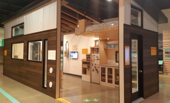 The tiny house at the Canada Science and Technology Museum from the exterior. Parts of the walls are missing to show the small kitchen and loft bed inside.
