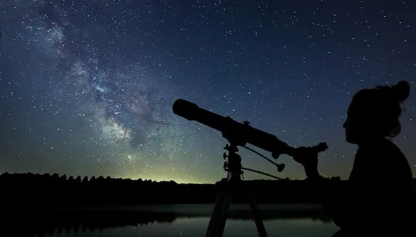 La silhouette d'une femme avec un télescope au premier plan regarde la galaxie de la Voie lactée dans le ciel nocturne
