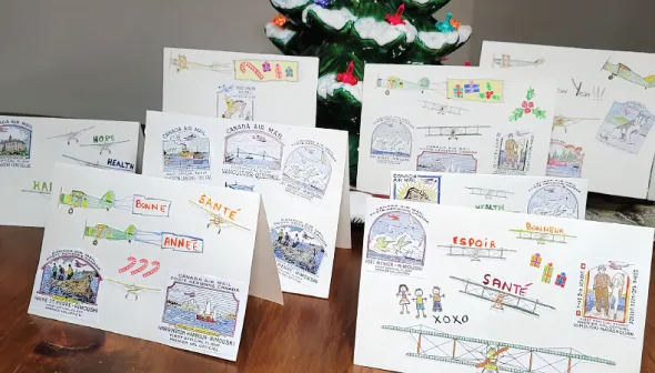 Huit cartes de vœux aux couleurs vives sont disposées sur une table de bois. Chaque carte présente des images différentes sur le thème de l'aviation. Les décors de Noël sont visibles à l’avant-plan et à l'arrière-plan de l'image.