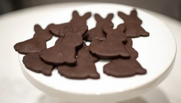 Dark brown cookies in the shape of rabbits are displayed on a raised, white platter. 