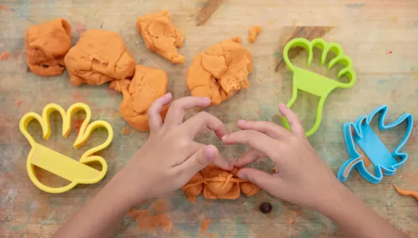 An aerial shot of a child's hands playing with orange playdough on a wooden surface. 
