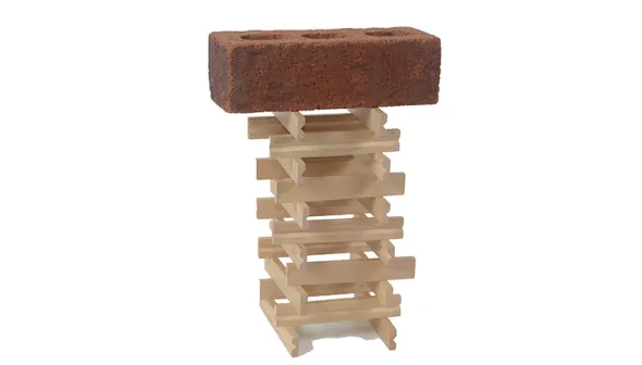 Des bâtons de bois sont empilés, deux par couche et en alternant la direction dans chaque couche pour former une tour à base carrée avec un centre creux. Une brique est posée au sommet de la tour.