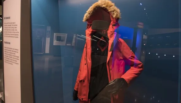A red winter coat with brown fur trim on the hood inside of a glass display case.