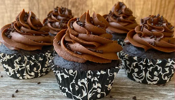 Rows of chocolate cupcakes are arranged on a wooden surface, with a wood background.