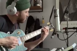 Homme jouant une guitare électrique bleue, devant micro et clavier.