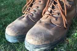A pair of worn-in brown boots stand on a patch of green grass.