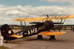 Biplan de taille moyenne avec des ailes jaunes distinctives, photographié dehors depuis l’angle arrière droit.