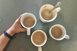 Four cups of tea rest on a kitchen counter top. A Brown hand reaches out to grab one of the tea cups.