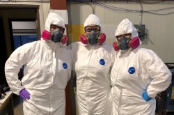 Three Conservators wearing personal protective equipment , including Tyvek suits, googles, nitrile gloves and respirators.