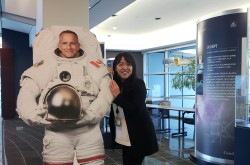 A young woman smiles and looks at the camera as she poses with a cardboard cut-out of Canadian astronaut David Saint-Jacques.