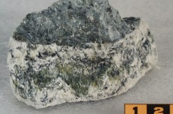 Asbestos in mineral form. The mineral is greenish and white in colour and there are visible strands of asbestos fibres. 