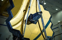 Un gros plan du miroir principal du télescope qui, vu de face, ressemble à un rayon de miel doré; devant lui, un miroir secondaire est replié.